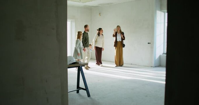 The realtor shows the house to a family with children. They walk around the room without decoration