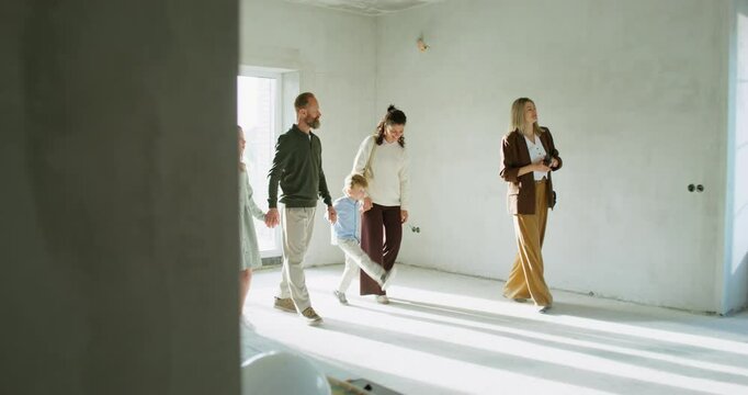 The realtor shows the house to a family with children. They walk around the room without decoration