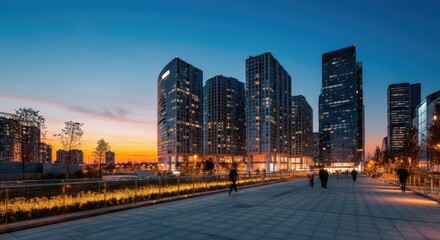 Obraz premium Cityscape at dusk with tall, illuminated buildings and people walking