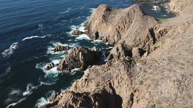 Flyover jagged sea rocks and foaming blue ocean in Baja California, MX