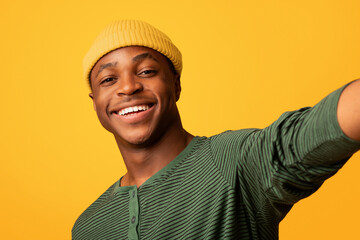 Happy Young Black Guy Taking Selfie While Posing Over Yellow Studio Background, Self-Portrait Of Cheerful Millennial African American Man Having Fun, Looking And Smiling At Camera, Closeup Shot