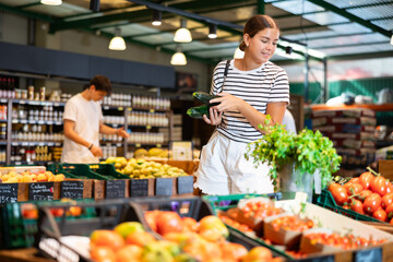 Young woman shopper choosing zucchini in grocery store