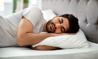 Comfortable sleep. Millennial arab man sleeping peacefully and see sweet dreams, lying in comfy bed and hugging pillow. Recreation, healthy male sleep, bedtime napping concept