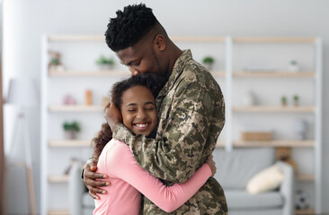 Side view of african american man in military uniform hugging child happy curly girl teenager at...