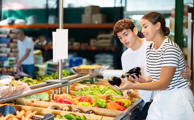 Young woman and young man shoppers choosing eggplants in grocery store