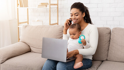 Happy African American Mother With Baby Infant Chatting On Phone Using Laptop Computer Sitting On Couch At Home. Maternity Leave, Modern Motherhood Lifestyle And Child Care Concept