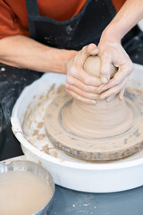 Close-up of a potter's hands working on a pottery wheel. Vertical photo. 