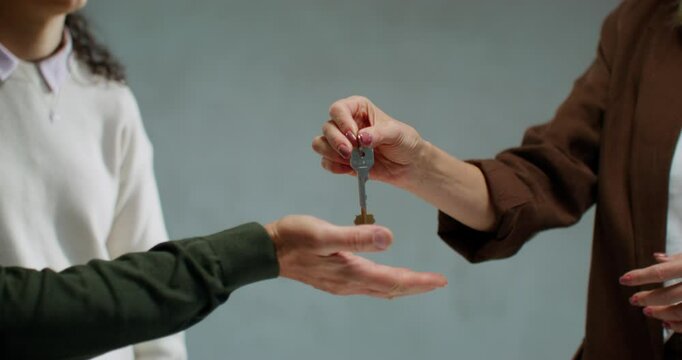 The realtor hands over the keys to the property to the buyers. Close-up of their hands, unrecognizable persons