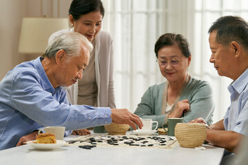 happy senior asian people playing game of go at home