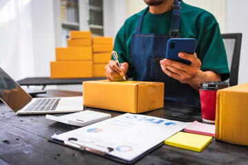 Close-up of a businessman’s hand packing items at a desk, preparing products for shipping. Highlighting delivery services for private companies online shopping with credit cards for convenience