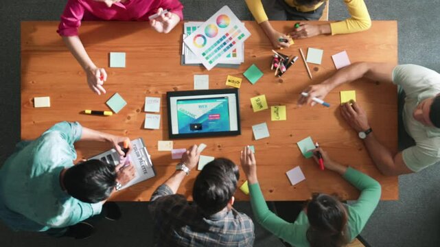 Top view of skilled business people working together to design web design. Aerial view of designer brainstorming and discussing about website interface for computer or digital application. Symposium.