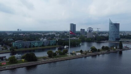 Latvian flag waving near modern district of Riga city, aerial view on moody day