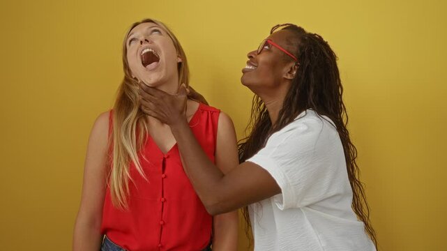 Women friends playfully choking over isolated yellow background