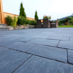 Close-up of dark gray slate patio paving stones, outdoors, shallow depth of field, backyard furniture blurred in background.