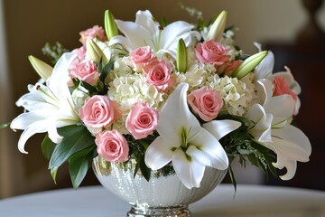 A beautiful centerpiece arrangement of pink roses, white lilies, and white hydrangeas in a silver bowl.