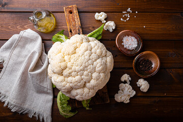 Raw whole cauliflower with seasonings on wooden background top view