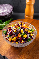  Fresh salad with red cabbage, carrots, hemp seeds and corn in a bowl on the table, vertical photo