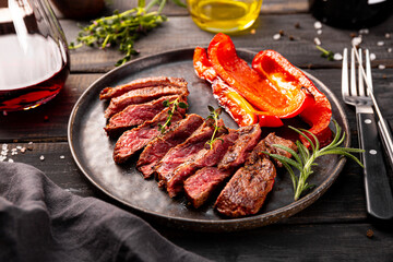 Grilled beef steak, well done with seasons and a glass of red wine on a black wooden background and plate close up