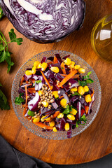  Fresh salad with red cabbage, carrots, hemp seeds and corn in a bowl on the table, vertical photo top view