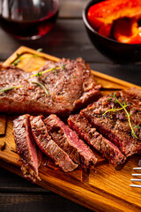 Grilled beef steak, well done with seasons and a glass of red wine on a black wooden background and cutting board close up