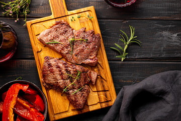 Grilled beef steak, well done with seasons and a glass of red wine on a black wooden background and cutting board top view