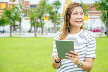 A professional woman checks her tablet while standing near the Grand Palace in Bangkok, blending work and travel.