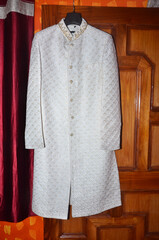 groom white color sherwani beside the wooden board in a room