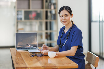 Female Asian female doctor or nurse sitting at laptop computer in clinic