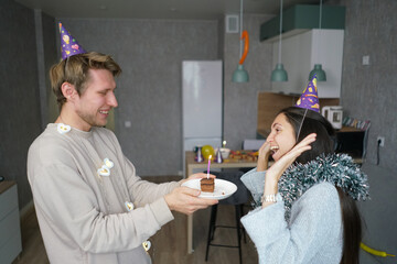 Couple smiles and embraces while celebrating with a cake and birthday hats in a cozy living room setting filled with decorations