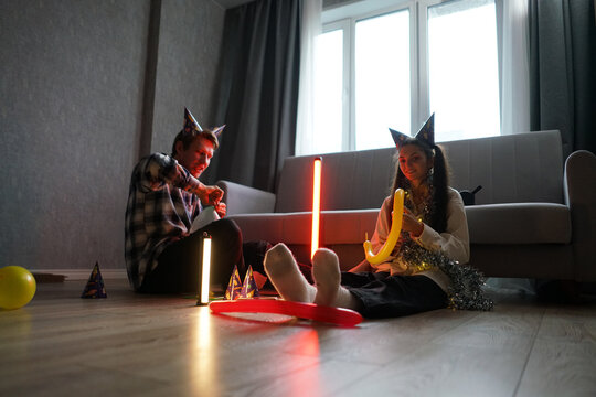 Couple enjoys a festive celebration on the floor, wearing party hats and surrounded by colorful decorations and balloons in a cozy indoor ambiance