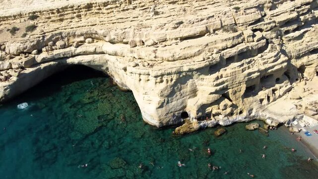 Aerial Orbit of Cliff Jumping Tourists in Matala Caves and Beach, Crete, Greece