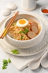 Noodle soup with chopsticks served in a textured white ceramic bowl, topped with boiled egg, sliced beef, and chopped scallions.