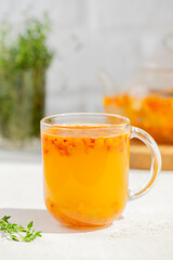 Sea buckthorn autumn tea with orange, thyme, honey and cinnamon in glass cups on white table. Herbal vitamin tea. Vertical orientation.