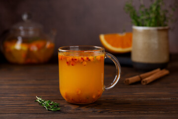 Sea buckthorn autumn tea with orange, thyme, honey and cinnamon in glass cups on wooden table. Herbal vitamin tea.