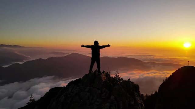 Impressive view of man watching sunset from mountain peak above fog and clouds.