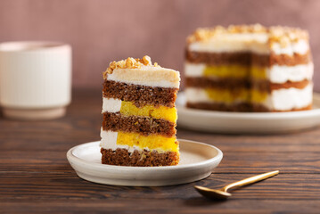 Piece of vegan pumpkin or carrot layered cake with coconut cream, nuts and orange confit with cup of tea on a table. Sugar, gluten and lactose free. Homemade dessert.