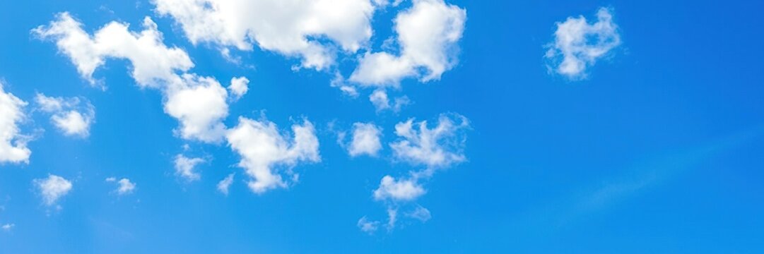 Softly scattered fluffy white clouds against a brilliant blue sky with just a few wispy strands, gentle weather, white clouds, blue sky