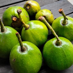A closeup shot of eight vibrant green avocados, showcasing their smooth skin and stems. Theyre arranged on a dark wooden surface, highlighting their natural beauty.