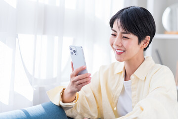 人物, 日本人, 女性, 携帯電話, 携帯, スマホ, 検索, 探す, ライフスタイル, マンション, 自宅, リラックス, 30代, ソファー, ネットショッピング, アプリ, スマートフォン, 若い, 家, 住まい, 住宅, 住居, 室内, 部屋, 座る, ひとり暮らし, 1人暮らし, ソファ, 20代, メール, 1人, コピースペース, sns, リビング, 笑顔, ショートヘア, カジュ