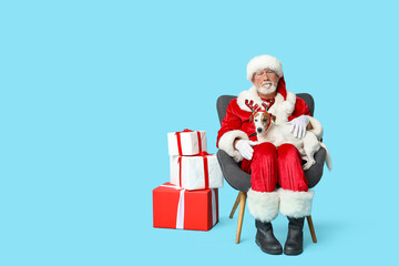 Santa Claus with cute Jack Russell Terrier dog in reindeer horns and Christmas gift boxes on blue background