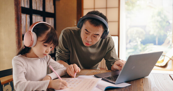 Asian dad, daughter and headphones with laptop for elearning, language tutoring or teaching at home. Japan, father or child writing with book or computer for online lesson or homeschooling at house