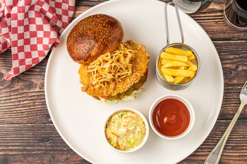 Chicken burger served with fries and sauces on a white porcelain plate