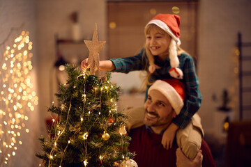 Close up of girl putting star on top of Christmas tree.
