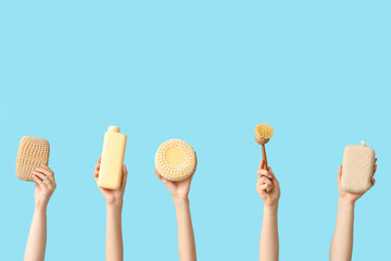 Female hands with bottle of cosmetic product, massage brush and bath sponges on blue background