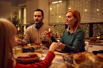 Mid adult woman praying with her family during Christmas meal at dining table.