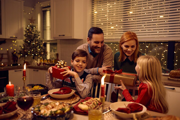 Happy parents surprising their children with Christmas presents during family dinner.