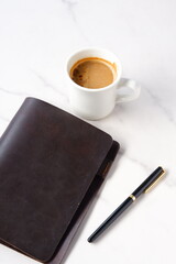 ミルクを入れたコーヒー、カフェ・ラッテを飲みながら、茶色の革のシステム手帳でデスクワーク中のイメージ
