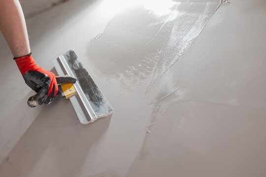 The hand of a craftsman with a spatula during work on leveling a wall with putty - painting work on preparing the surface before finishing and painting