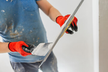 The hand of a craftsman with a spatula during work on leveling a wall with putty - painting work on...