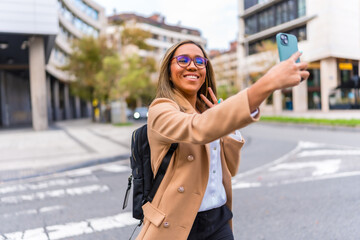 Fototapeta premium Happy latin businesswoman taking selfie standing in the city